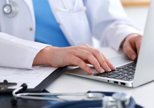 Photo of a physician's hands typing on a keyboard; stethoscope on desk
