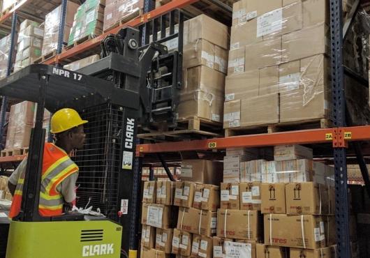 A man operates a forklift loaded with boxes in a warehouse.