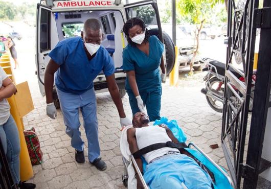 Two emergency clinicians wheel a  man on a gurney from an ambulance into a hospital entryway in Haiti