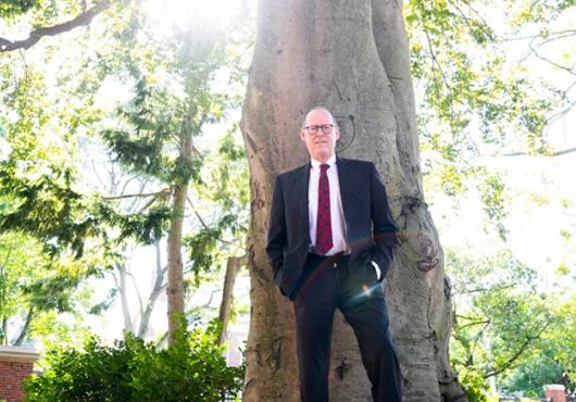 Paul Farmer stands against the front of a tall tree.