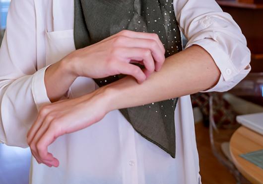 Muslim woman with 3/4 length sleeves scratching arm; image cropped to just show torso