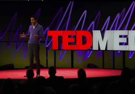 A man speaks on a stage, standing in front of a sign that says TEDMED.