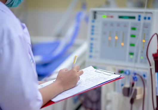 nurse with clipboard checking dialysis machine