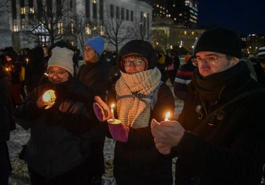 People outdoors on a snowy night wearing warm clothes and holding glowing candles