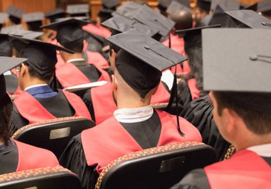 View of back of master's graduates in graduation attire seated in martin conference center