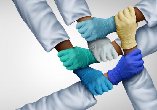 Photo of five gloved hands grasping alternating forearms of different skin colors