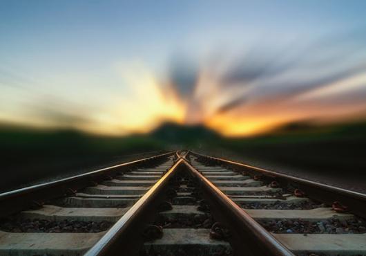 Two train tracks merge in a blurry sunset.