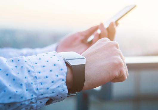 A person's hands, wearing a smart watch and holding a smart phone.
