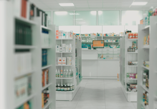 Shelves filled with medications in the aisles of a pharmacy draw the eye to the pharmacist’s prescription counter.