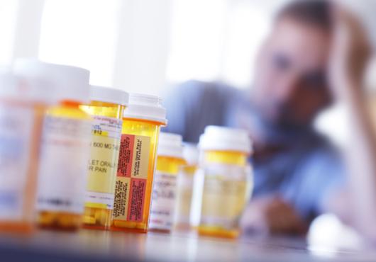 A blurry man in the background behind a row of prescription drugs.