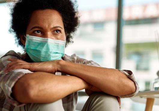 A woman wearing a surgical masks sits with her arms crossed