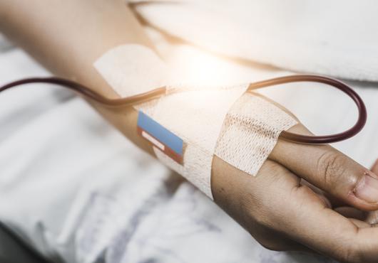 Close-up of a hospital patient's hand with a bandage and an IV tube. 
