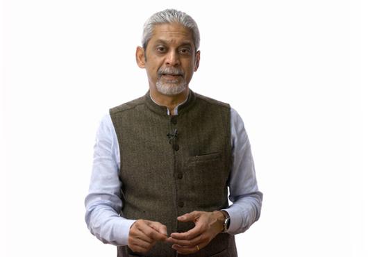 Gray-haired South Asian man in a vest and button-down shirt
