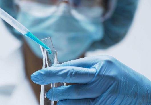 Person with mask and gloves pouring liquid into a test tube
