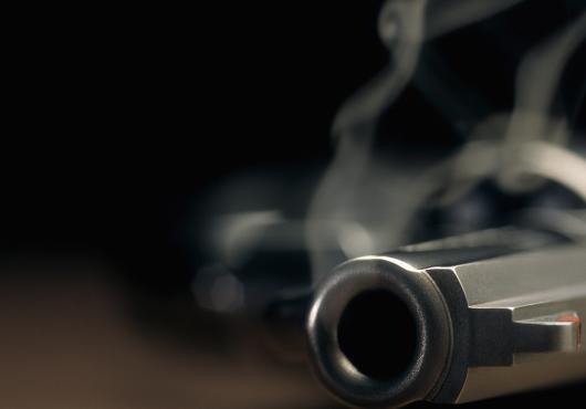 Narrow focus on the barrel of a smoking gun lying on the floor.
