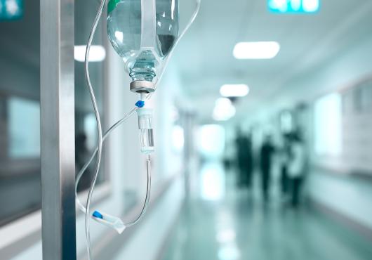 A bag of IV medicine hangs in a lonely hallway.
