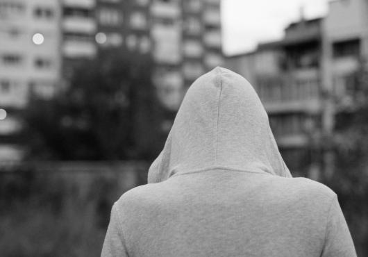 Black & white photo of person in a hooded sweatshirt, back facing camera in an urban setting