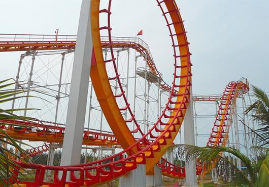 a roller coaster loops around in foreground, then rises and falls in the distance