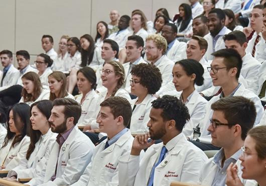large group photo in auditorium of new students in white coats