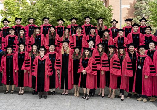 dozens of doctoral recipients stand outside with program head and graduate dean