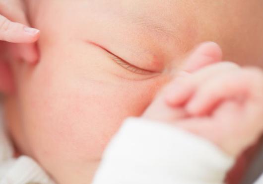 Closeup of a baby's face with one eye closed and hand resting on nose