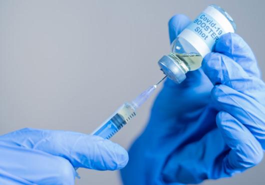 Hands in protective gloves putting a needle into a COVID-19 booster vaccine vial