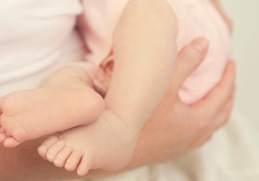 Photo of someone holding an infant, only the baby's feet and legs shown