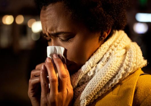 Closeup of woman in hat and scarf blowing nose into a tissue