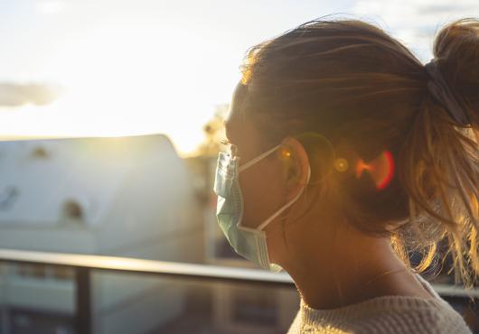 A woman  wearing a mask is seen in profile, backlit by the sun.