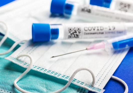photo of medical mask, vials marked covid-19 and needle