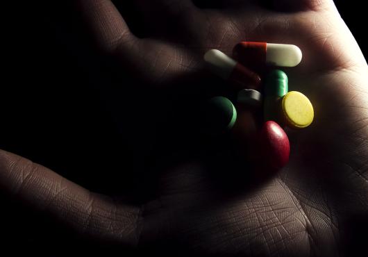 A shadowy hand holds a variety of pills.