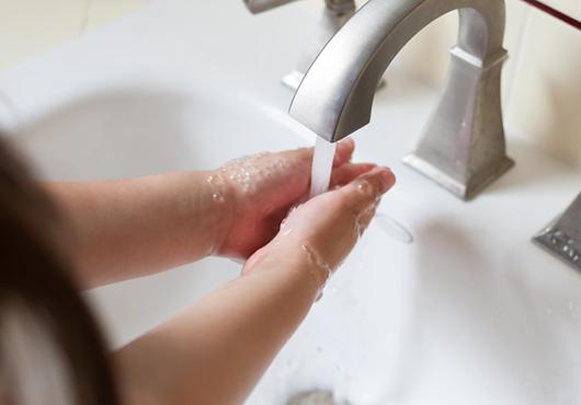 photo showing arms of female child washing hands under faucet with running water