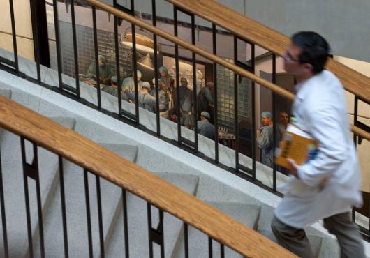 A student in a white coat runs up stairs