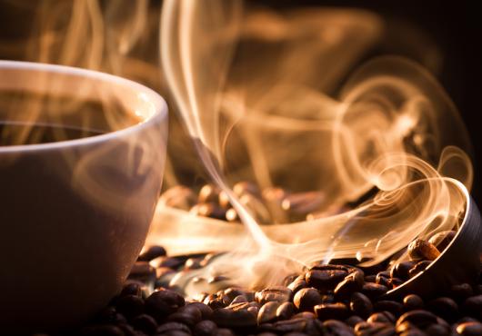 Steaming mug of coffee atop coffee beans