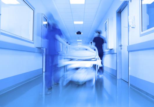 Hospital hallway with blurred figures & gurney.