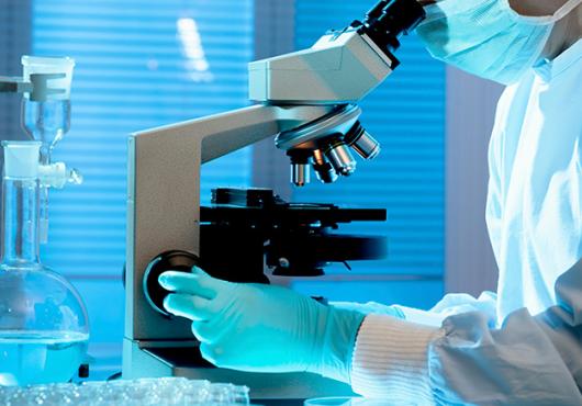 person at microscope in full PPE, face cropped out