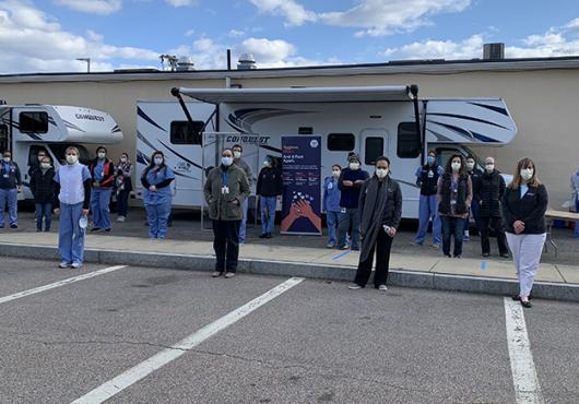 people wearing masks stand 6 feet apart in a parking lot with two RVs in background