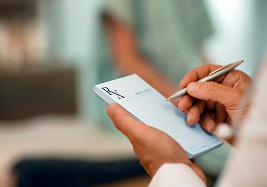 Doctor using a pen to fill out a prescription pad.