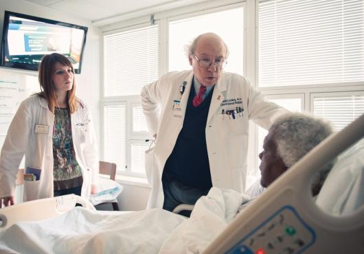 Two doctors talk to a patient in a hospital room