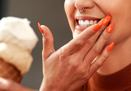 Cropped image of woman eating an ice cream cone and flinching and holding hand to mouth like in pain