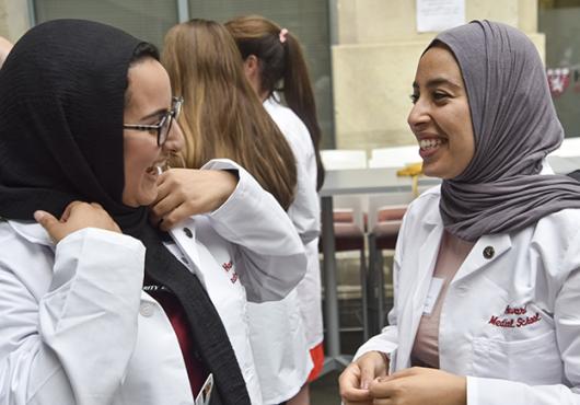 Two HMS students in Class of 2023 chat with white coats on.