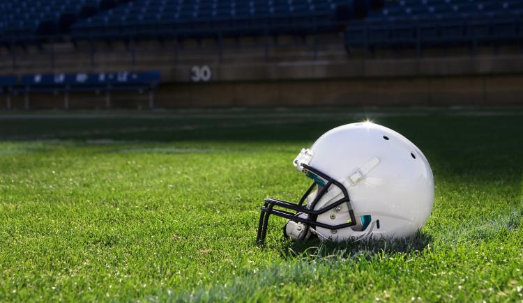 A white football helmet rests on a grass field in a stadium