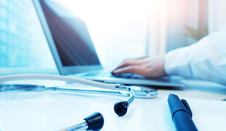 Close-up of a laptop, stethoscope, and physician’s forearm in white coat