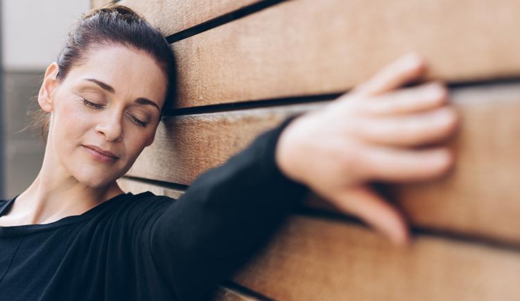 a woman with eyes closed leans her head and her outstretched hand on a wall