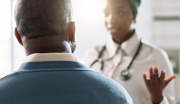 A photograph of a doctor (with face out of focus) talking with her patient, who has his back to the camera.