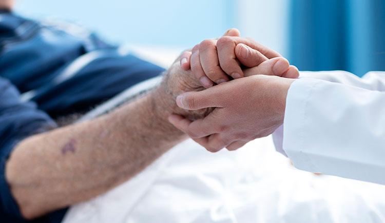 Close up of doctor in white coat holding the hand of an elderly patient