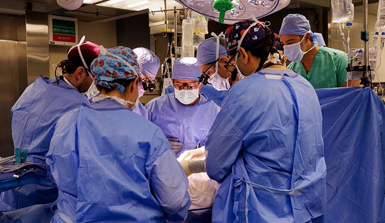 Eight people in surgical garb cluster around an operating table