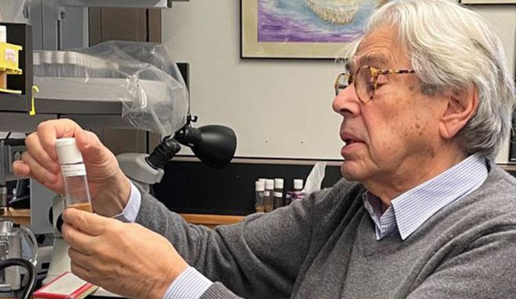 A professor sitting at a lab bench looking at a small plastic container