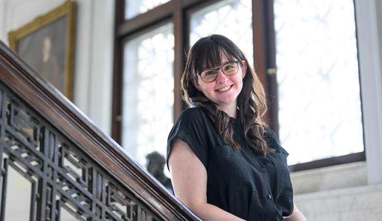 A woman leans on a banister and smiles at the camera