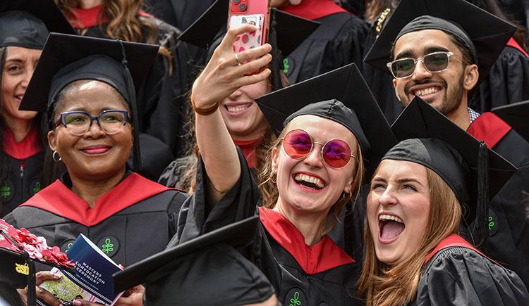 A woman holds up a cell phone to take a selfie with several other people.